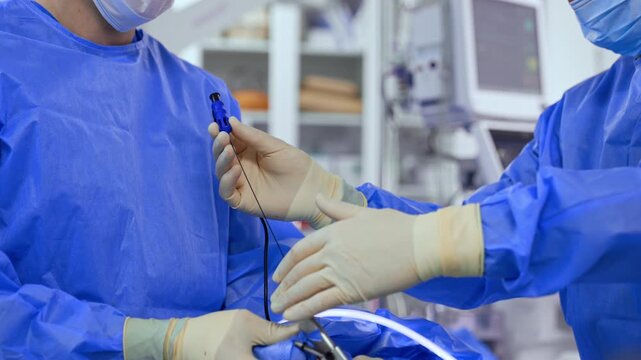 Unrecognized doctors, wearing blue robes and white latex gloves use advanced medical devices and tools. Performance of modern neurosurgical operation in the hospital.