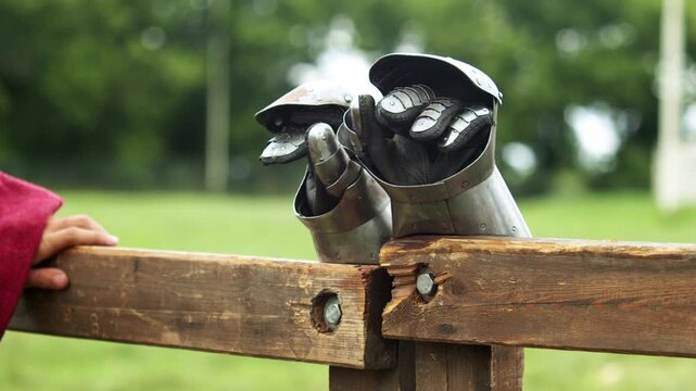 Detailed macro view showcases articulated steel finger plates, leather undergloves, and rivets of knightly mitten gauntlets resting on wooden lists barrier before combat.