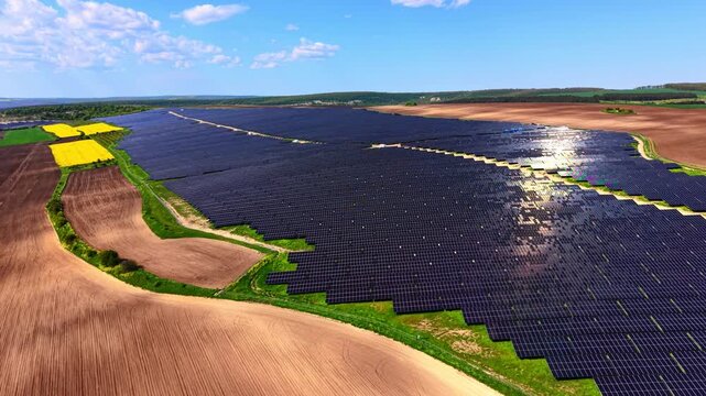 Aerial view of solar panel field bordering plowed land. Drone angle shows panel array beside yellow rapeseed patch and brown farmland.