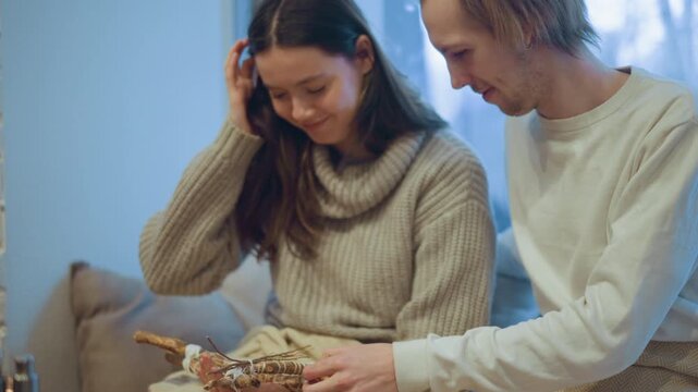 Close up of two people examining decorative object together in soft indoor lighting. woman and man sit closely both focused on item held by her hands while man assists or observes. scene