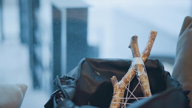 Close up of small dreamcatcher made from twigs and string resting in outdoor bag during snowfall. background shows falling snow with blurred trees creating wintery atmosphere