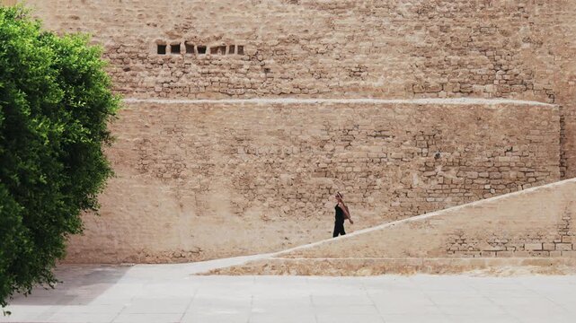 Woman walking alongside ancient Ribat walls in Monastir, Tunisia, with serene atmosphere