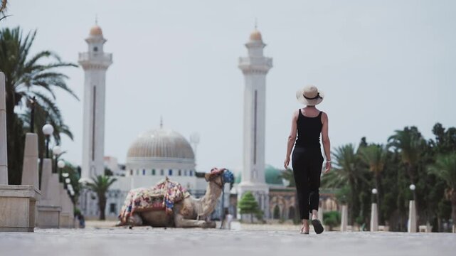 Woman sightseeing Monastir near a Mausoleum Habib Bourguiba with a camel in Tunisia