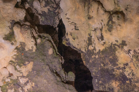 ​Horizontal close up photo of deep natural rock crevice and textured limestone wall inside mountain cave with mineral patterns and dark cavern opening fissure