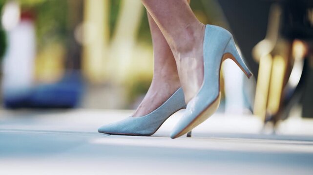 Close-up of a stylish woman in elegant high heels outdoors making shy gesture rising leg up in the air
