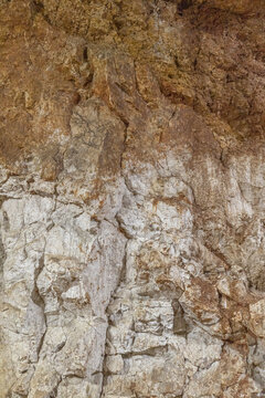 Vertical close up photo of rough natural cave rock wall texture with brown and white limestone layers and mineral formations for background design project