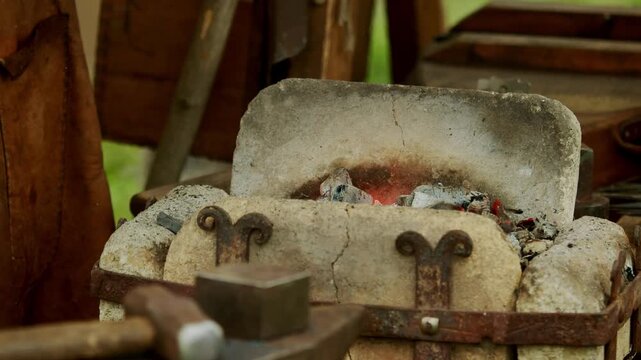 authentic portable stone furnace reinforced with wrought iron brackets, filled with glowing hot embers, rising smoke, and flickering flames during historical craft fair.