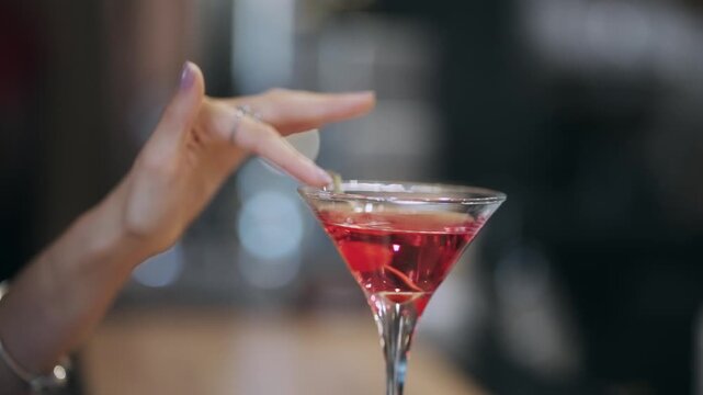 Woman hand with delicate fingers adorned with rings, gracefully tracing the rim of a red cocktail in a bar