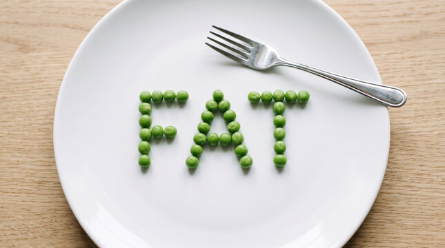 Peas arranged to spell the word fat on a white plate with a metal fork. Conceptual image about eating disorder, body dysmorphia, weight concerns, and unhealthy food relationship habits.