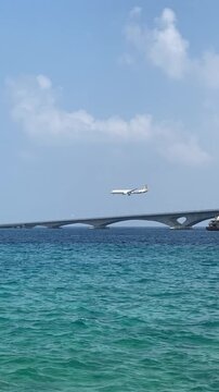 Vertical video of a commercial passenger airplane landing at Velana International Airport over the Sinamale Bridge and ocean in Male, Maldives.
