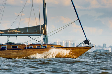 Obraz premium Vintage sailing boat through splashing water at sunset, Sailing regatta in the Gulf of Finland at sunset, hot race of several yachts, teamwork