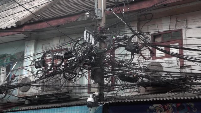 Messy power wires are tangled on the electrical pole, creating a chaotic arrangement of internet cables and powerlines in Thailand.