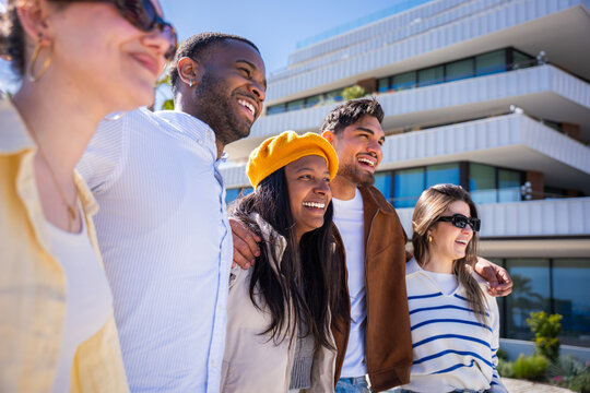 Cheerful friends enjoy a walk together in a clean modern residential area with contemporary buildings, sharing a relaxed social travel moment.
