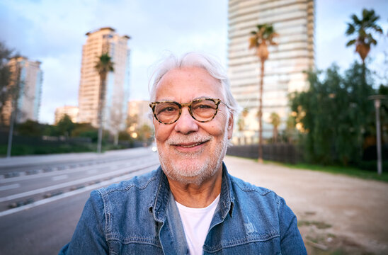 Elegant senior man looking at the camera with stylish glasses confidently in a modern city at dusk, enjoying her retirement and urban lifestyle
