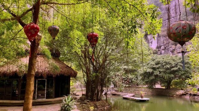 Traditional Red Silk Lanterns Hanging in Lush Garden with Thatched Cottage in Ninh Binh Vietnam