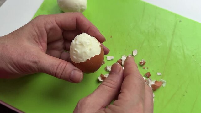 Peel boiled egg. Person hand removes egg white from shell in kitchen during cooking. Woman peeling boiled egg for breakfast. Person is carefully taking out egg white from cracked eggshell in kitchen. 
