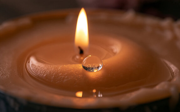 A close-up shot of a burning candle with a single drop of water resting on its surface