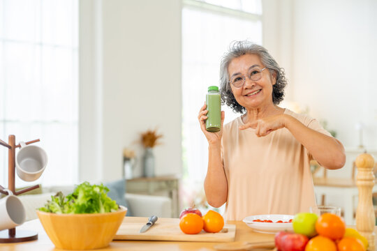 Asian senior woman eating healthy food and drinking fresh green vegetable juice at home. Elderly nutrition balanced diet, wellness aging lifestyle with natural ingredients and healthy daily routine