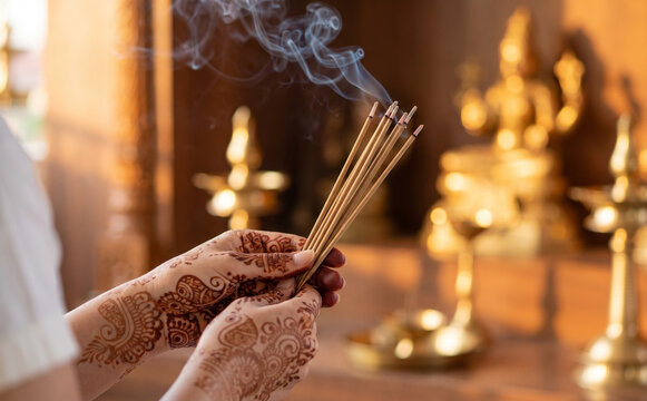 Young Indian woman holding burning incense sticks with traditional mehndi henna tattoos for prayer ritual