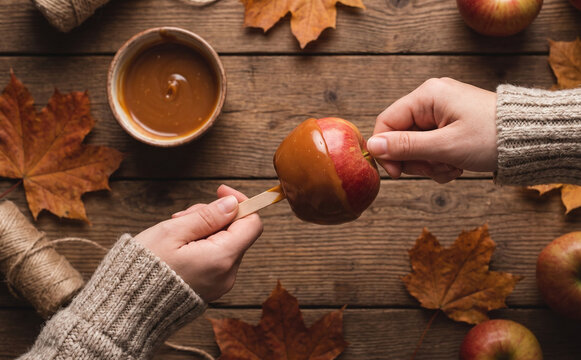 Making caramel apples in autumn with wooden table, maple leaves, and caramel sauce