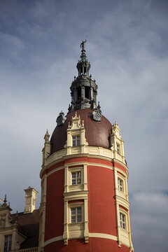 Vertical shot focusing on the intricate reddish dome, carved windows, spire, and statue at the top of the main tower of Muskau Castle.