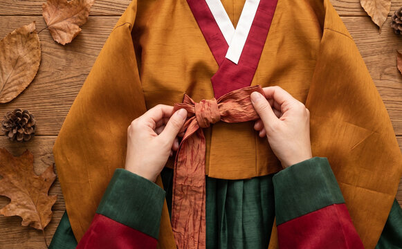 Traditional Korean hanbok being tied by hands on a wooden background with autumn leaves for cultural heritage concepts