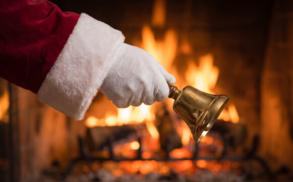 Santa Claus ringing a golden hand bell in front of a warm fireplace for Christmas celebration