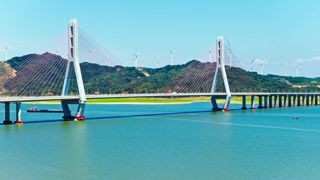 Cable-stayed bridge spanning across Poyang Lake with wind turbines on hills in Jiujiang, China.