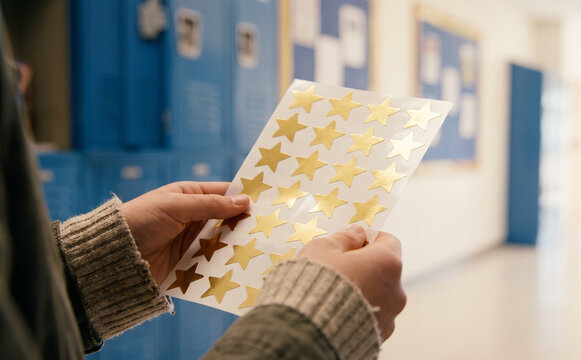 Child holding a sheet of golden star stickers in a school hallway, representing achievement and reward concepts