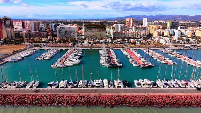Marina harbor view in Castellon, Valencia, Spain. Elevated drone angle of docked sailing boats, blue water and coastal city buildings.