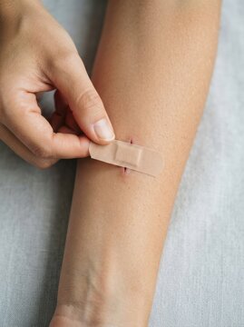 Woman applying adhesive bandage on cut wound on her arm for first aid treatment and healing process