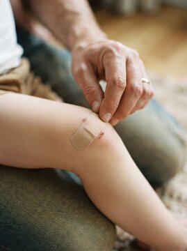 Adult applying adhesive bandage to child knee scraped in minor playground accident representing care