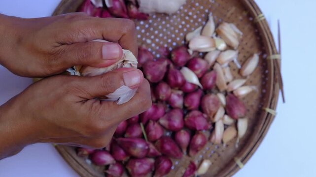 Close up of hands peeling shallots and garlic cloves with knife on a plate, traditional cooking preparation