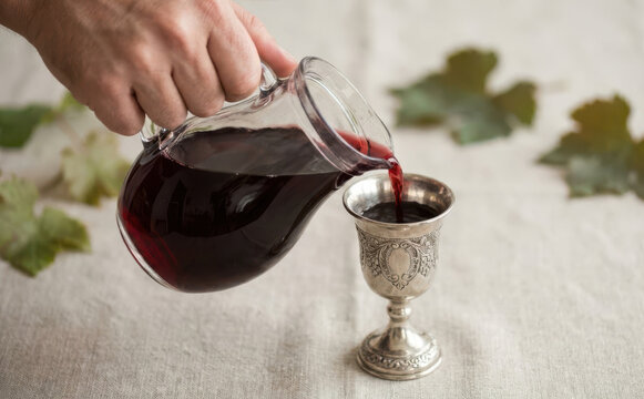 Pouring red wine from a glass pitcher into a traditional silver kiddush cup for Passover celebration