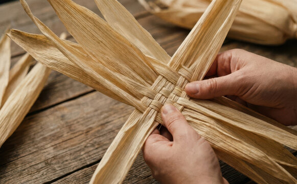 Hands weaving traditional corn husk craft on wooden rustic table background for harvest decoration