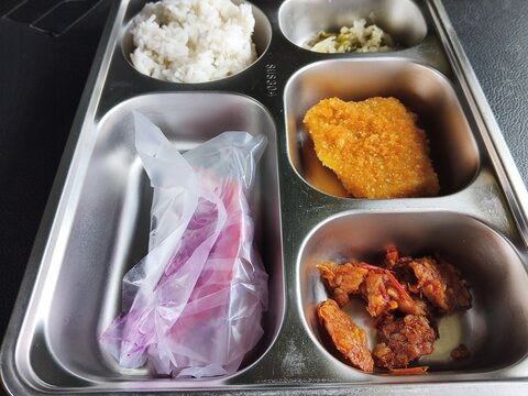 Meal served in a metal tray containing rice a fried cutlet and meat portions with additional
