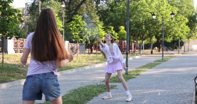 Happy teenage girls with rackets and shuttlecock playing badminton outdoors