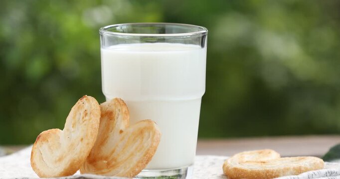 Fresh milk in glass and palmier cookies on wooden table, closeup. Camera moving right
