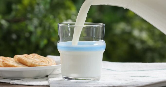 Woman pouring fresh milk into glass at wooden table, closeup