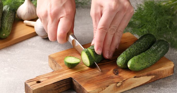Woman cutting fresh cucumber at gray table, closeup