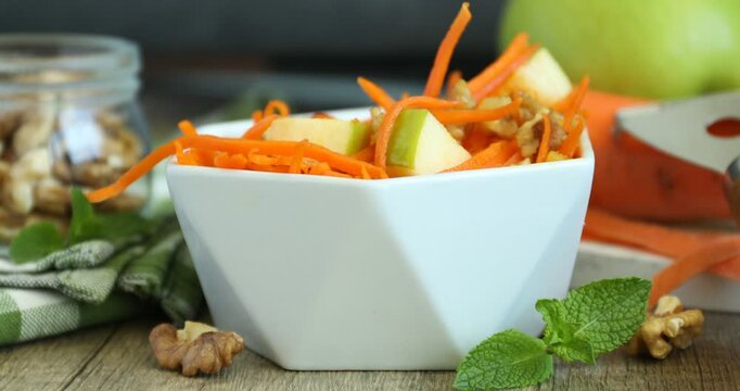 Eating delicious carrot salad with apple, walnuts and mint at wooden table, closeup