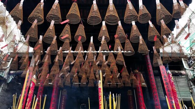 Smoke rising from traditional incense sticks in an ornate burner surrounded by hanging spiral incense coils in a historic Chinese temple, Cholon, District 5, Ho Chi Minh City, Vietnam