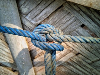 Strong blue rope knot highlighting rough texture and security, with a blurred woven bamboo wall in the background. © Super