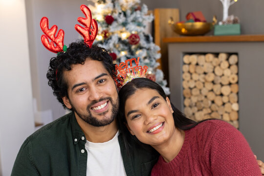 African American couple smiling, leaning on sofa at home with red sweater and reindeer headbands