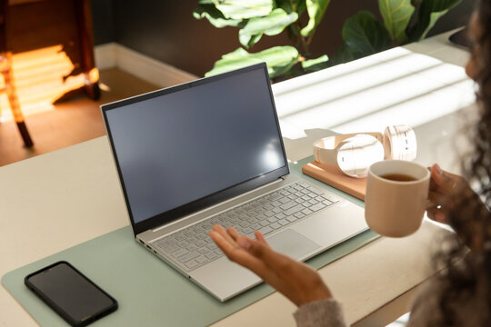 Silver laptop is sitting on pale desk mat by window with headphones and mug nearby