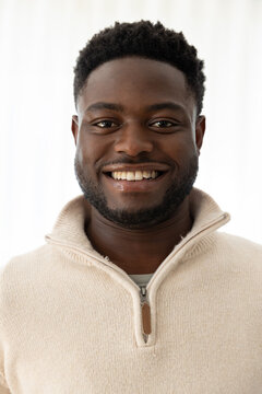African adult male smiling, facing camera, wearing tan half-zip sweater with leather tab in studio