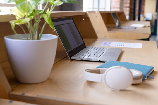 Silver laptop is showing spreadsheet on long bench near windows with planter, headset