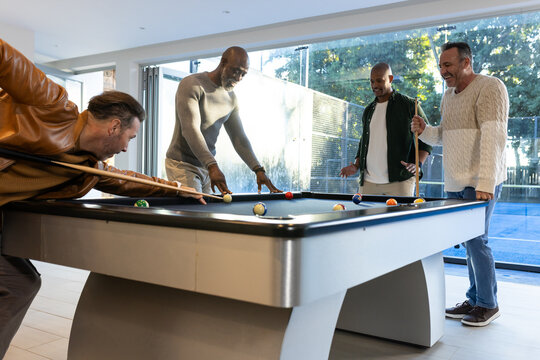 Diverse male friends playing pool in modern game room around blue felt table and cues