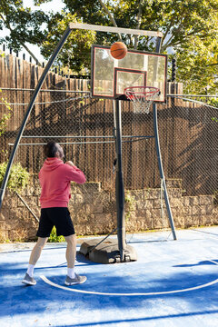 Adult man shooting basketball on backyard blue half-court at portable hoop with red rim