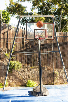 Portable basketball hoop standing on blue court in backyard, orange basketball hovering above rim
